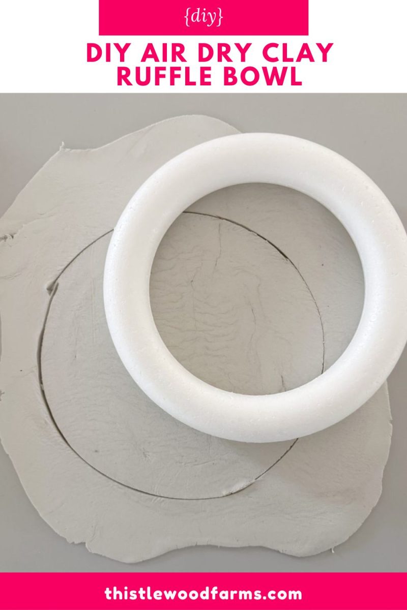 a round piece of white clay with a circular shape cut into it, a white foam ring placed on top, and a pink banner that reads "diy air dry clay ruffle bowl" at the top.