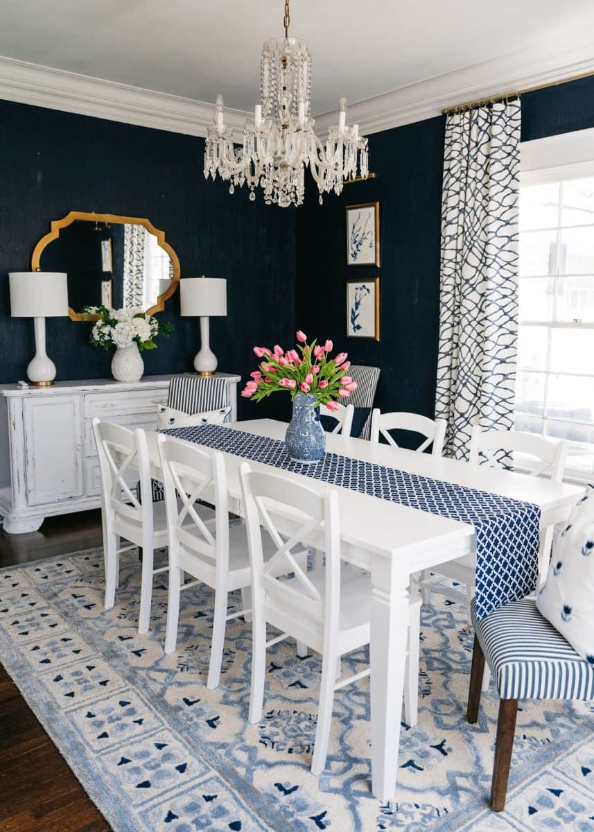 how to mix patterns with blue and white 4 elegant dining room featuring a white table with patterned blue tablecloth, matching white chairs, a classic crystal chandelier, deep blue walls adorned with art, and a complementing blue patterned rug.