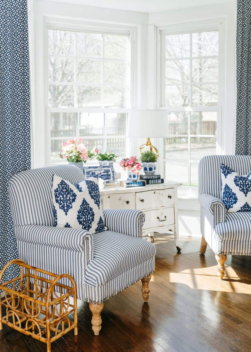 how to mix patterns with blue and white 7 a bright and inviting living room corner with natural light flooding in through large windows, featuring two striped armchairs with matching blue and white patterned cushions, a small vintage dresser adorned with floral arrangements, and a woven wicker basket by the side, all complemented by elegant blue patterned curtains.
