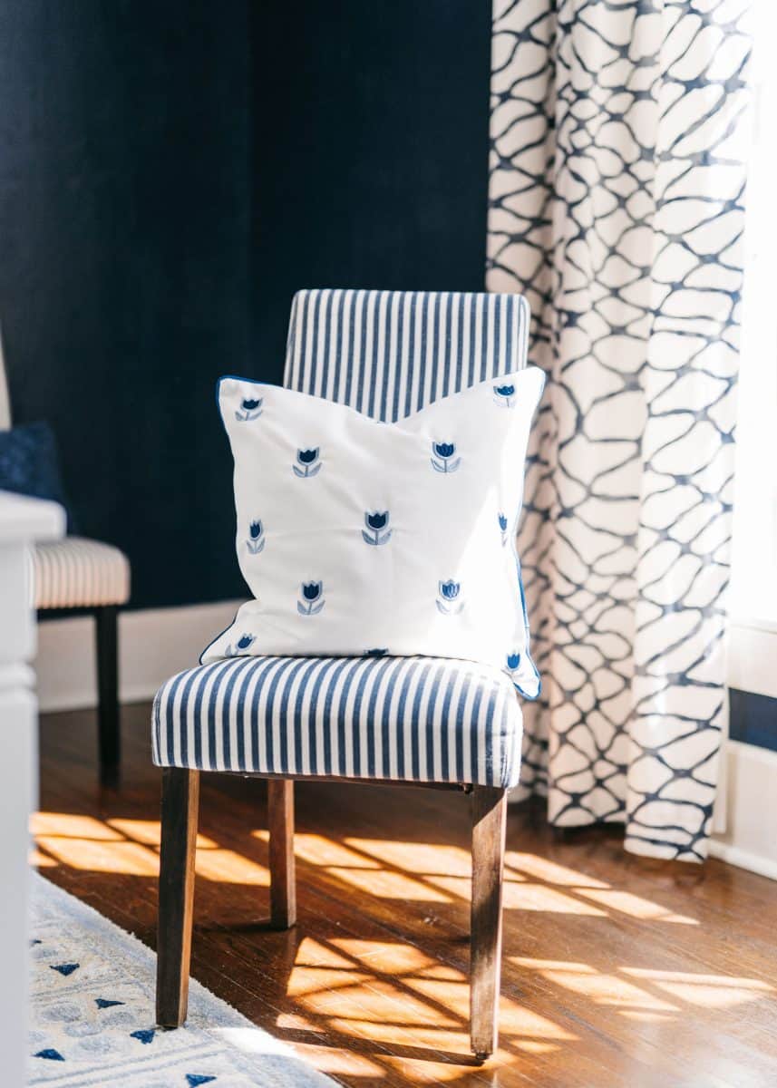 how to mix patterns with blue and white 11 a cozy nook featuring a stylish striped chair with a nautical-themed pillow, flanked by a dark blue accent wall and a window draped with patterned curtains, bathed in warm sunlight.
