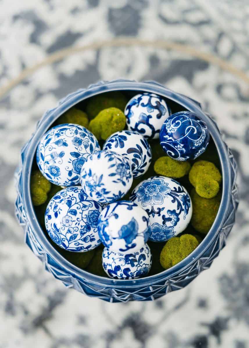 how to mix patterns with blue and white 6 a decorative bowl filled with intricately painted blue and white eggs, nestled among mossy green spheres, set on a patterned gray and white background offers creative decorative bowl filler ideas.