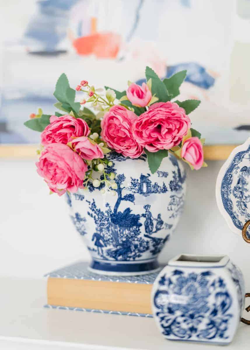 how to mix patterns with blue and white 8 a blue and white porcelain vase with intricate designs holds a bouquet of bright pink roses and greenery, placed on a closed book next to a matching decorative jar.