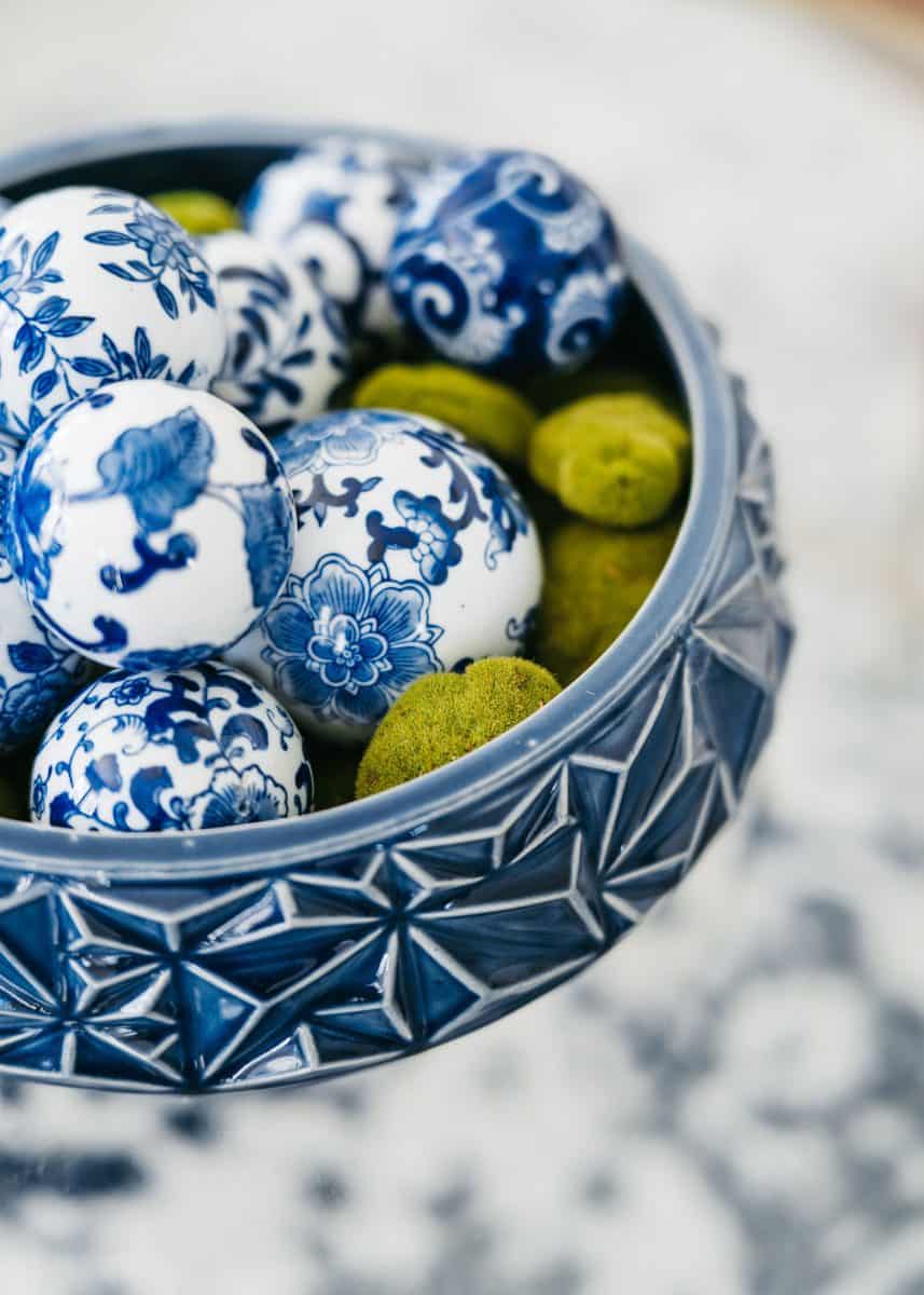how to mix patterns with blue and white 12 a decorative bowl filled with intricately painted blue and white ceramic balls alongside green textured spheres, sitting on a patterned surface.
