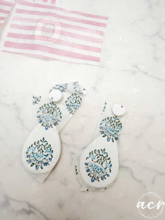 how to use uv resin and decoupage earrings 95 two pieces of white fabric with blue and green floral patterns cut into ornament shapes lie on a marble surface, perfect for creating decoupage earrings. in the background, pink and white striped fabric pieces await their own uv resin finish.