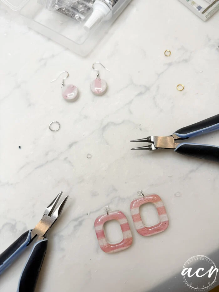 how to use uv resin and decoupage earrings 105 a marble surface with jewelry-making tools, decoupage earrings in pink and white, jump rings, and a small open organizer with supplies. the scene suggests a diy jewelry crafting project, perfect for exploring how to use uv resin.