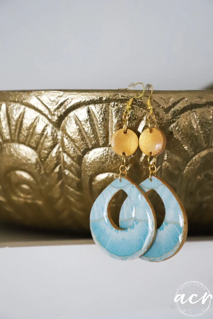 how to use uv resin and decoupage earrings 111 a pair of handmade decoupage earrings with gold round beads and large, oval-shaped blue uv resin drops hang in front of a textured gold decorative surface.