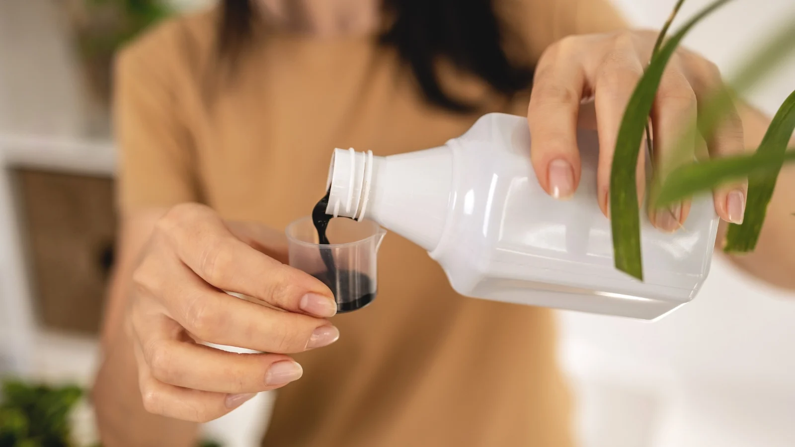 a person wearing a light-brown shirt, pouring liquid fertilizer in a smaller container
