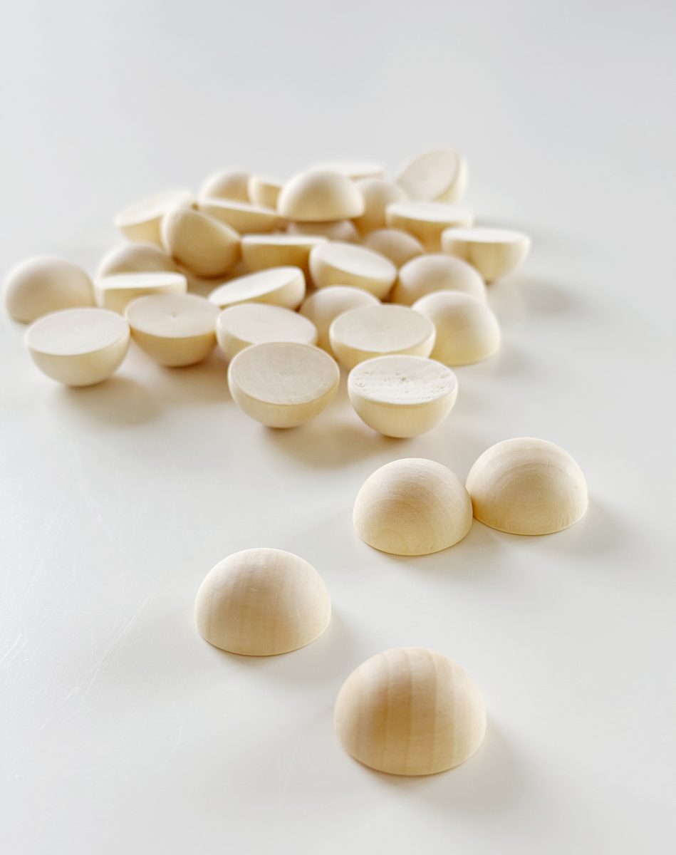 diy hobnail vase that looks like vintage milkglass 33 several small, smooth, light wooden half-spheres are scattered on a white surface, with some in the foreground and a pile clustered in the background.