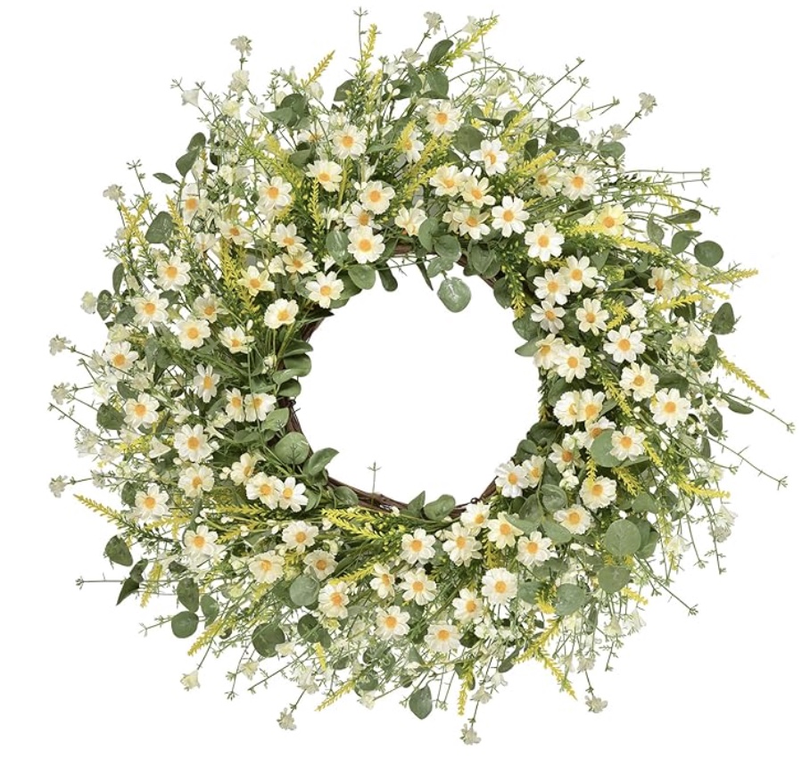 a circular wreath made of green leaves and small white and yellow daisy-like flowers, arranged densely in a natural, airy style against a white background.