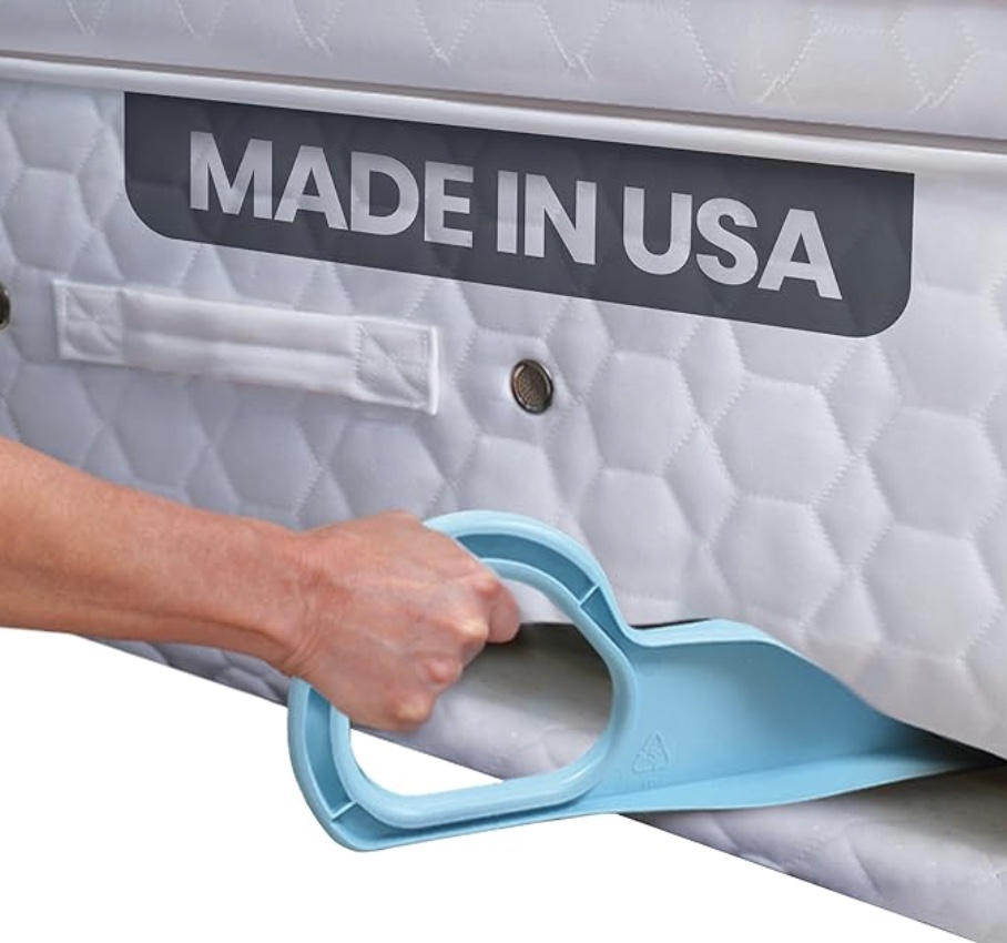 a hand uses a blue plastic tool to lift a mattress with a white quilted surface and a visible "made in usa" label. the tool helps make lifting the mattress easier.