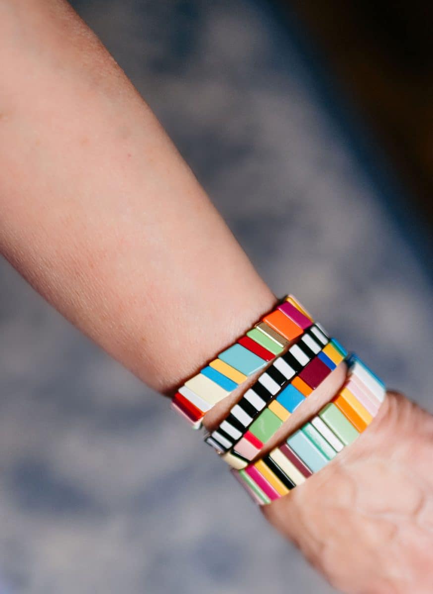 a person wearing three colorful, geometric-patterned bracelets on their wrist. the bracelets feature a variety of colors, including blue, red, yellow, black, and white, with distinct rectangular and square shapes. the background is blurred.