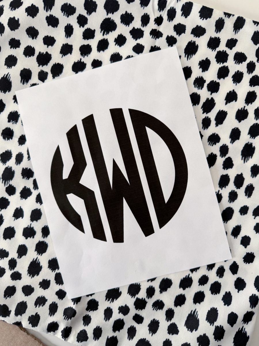 a white paper with the bold black letters "kwd" in a circular monogram design, placed on a fabric with a black and white irregular polka dot pattern.