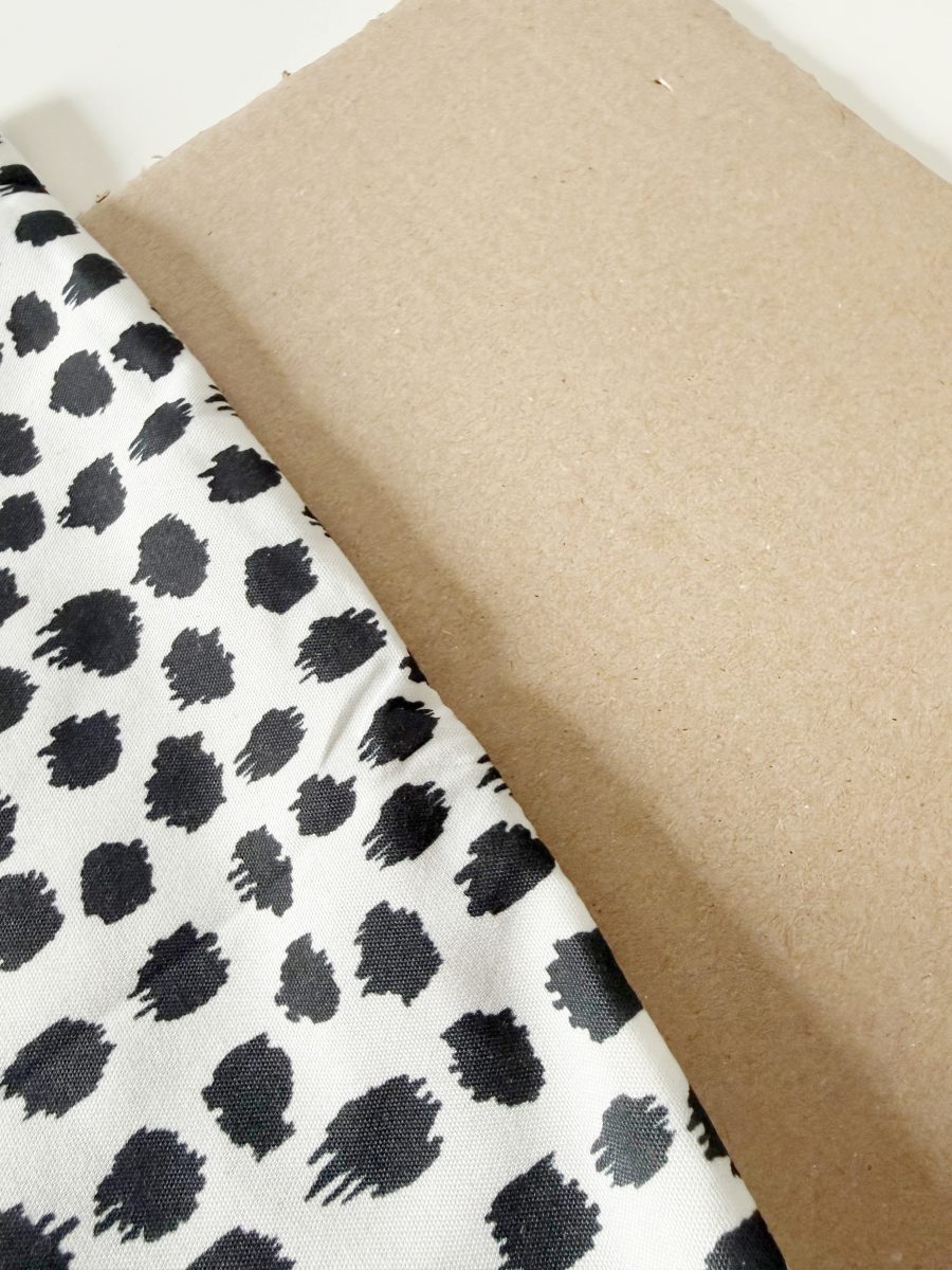 a piece of fabric with a black and white spotted pattern lies partially over a sheet of plain brown cardboard. the fabric appears slightly wrinkled.