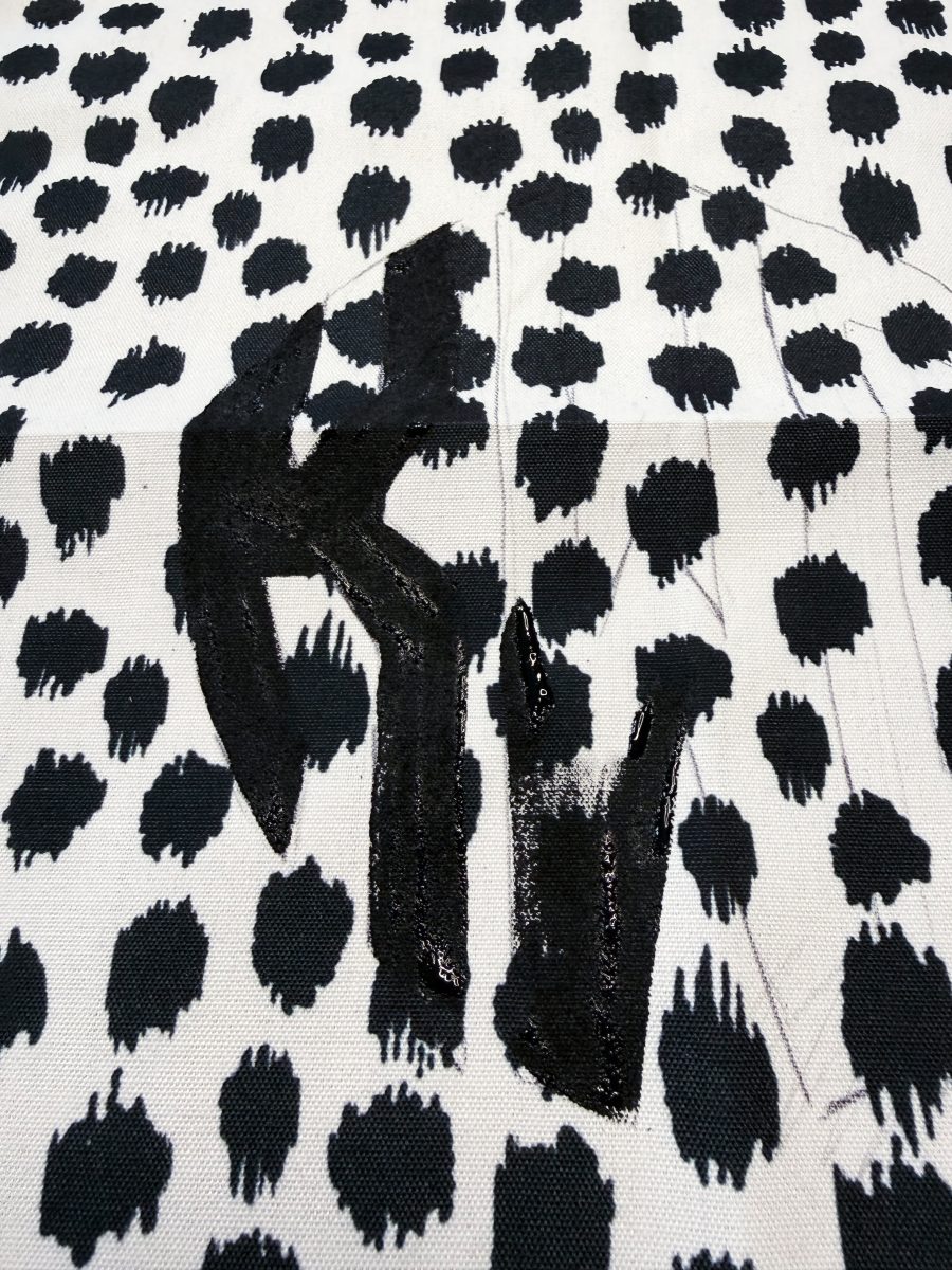 a textured black "kw" design is stitched onto a white fabric with a bold black irregular dot pattern. the letters have an uneven, hand-painted appearance and glossy finish, standing out against the spotted background.