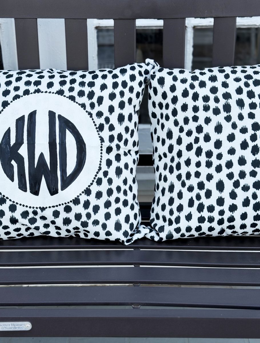 two white throw pillows with black polka dot patterns rest on a dark wooden bench. one pillow features a circular design with the initials "kwd" in bold black letters.