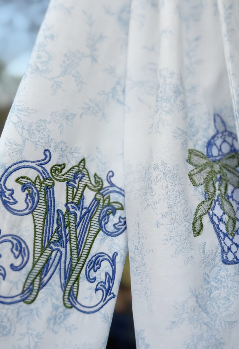 7 easy front porch decor ideas for spring 11 white fabric with blue floral patterns features ornate blue and green embroidered initials "hw" on the left and a blue and green embroidered vase with a bow on the right. the background is softly blurred.