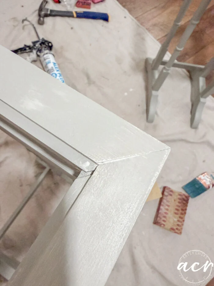 a close-up of a freshly painted, light-colored wooden frame corner, with painting and sanding supplies scattered on a drop cloth in the background—perfect inspiration for refurbishing glass top tables or stylish nesting tables.