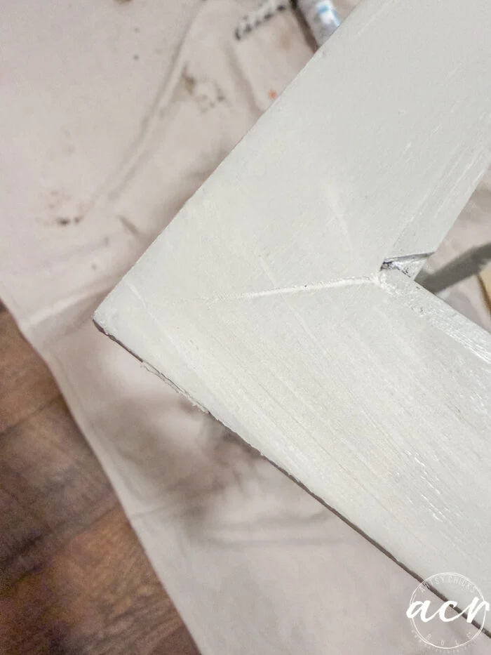 a close-up of a light-colored wooden table corner with a visible crack running through it, resting on a cloth drop sheet over a wooden floor—perfect for pairing with glass topped nesting tables in any stylish space.