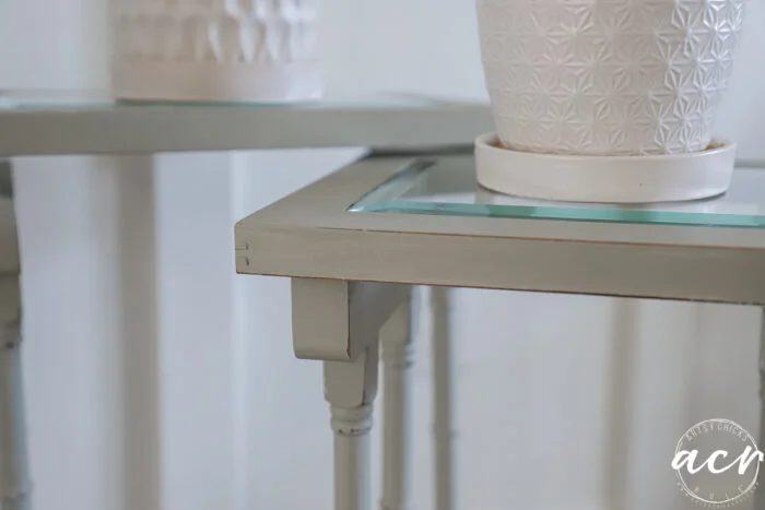close-up of two light green glass topped nesting tables with slightly distressed edges. each table holds a white textured plant pot, while the softly blurred background enhances their charm.
