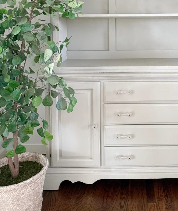 7 simple steps to style a hutch 34 a large white cabinet with empty shelves and drawers stands against a white wall. a potted green leafy plant is to the left, and a vintage white decorative box sits on top—an inviting spot to style a hutch on wooden floors.