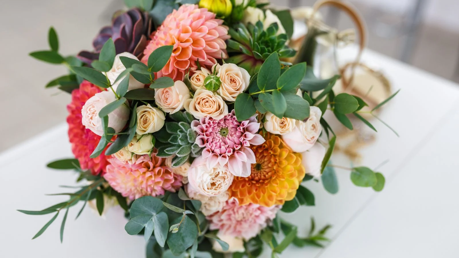 an overhead and close-up shot of an arrangement of dahlia blooms, placed on a white surface outdoors