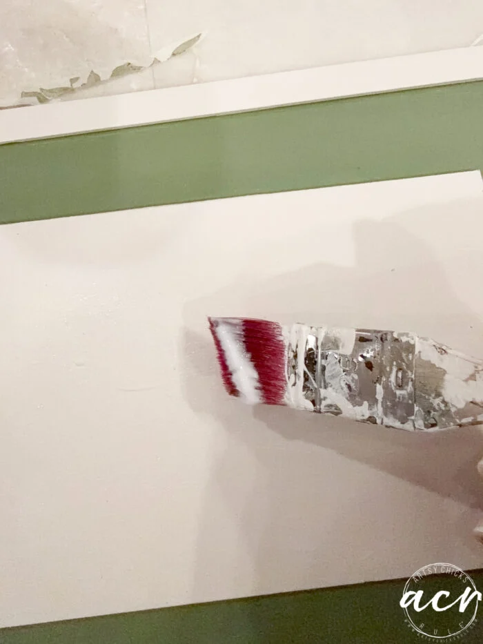 a paintbrush with white paint is being applied to a flat white surface in this easter edition image. the background shows a green and white area, and a watermark with the text “acv” appears in the bottom right corner.