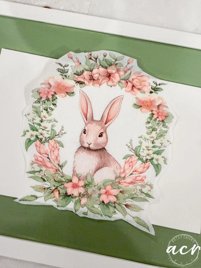 a watercolor illustration of a brown rabbit sits in the center of a floral wreath made of pink flowers and green leaves, displayed on a white and green background—perfect for the flipping smalls easter edition.