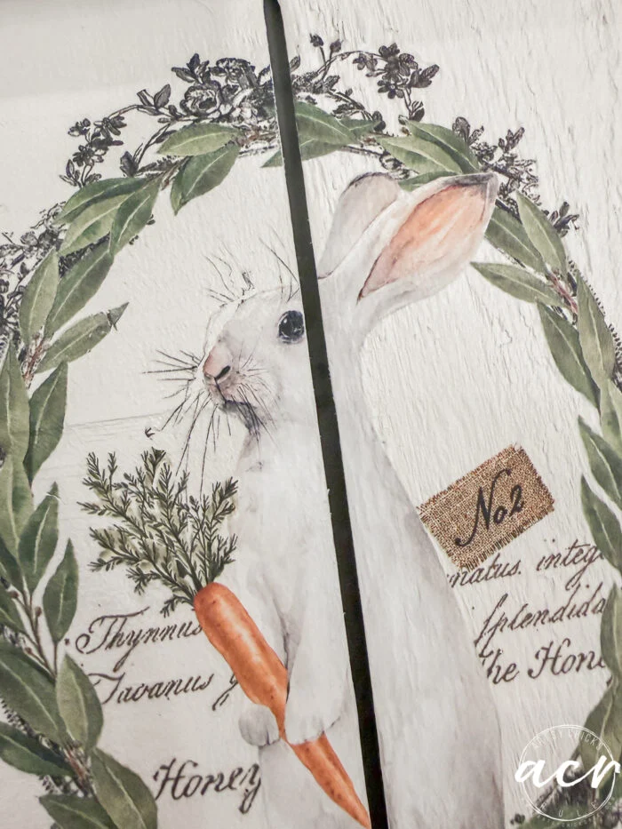 a white rabbit holding a carrot is illustrated inside a green leafy wreath, with vintage-style text and the label no 2 in the background. the image, part of the flipping smalls easter edition, is split by a narrow black gap.