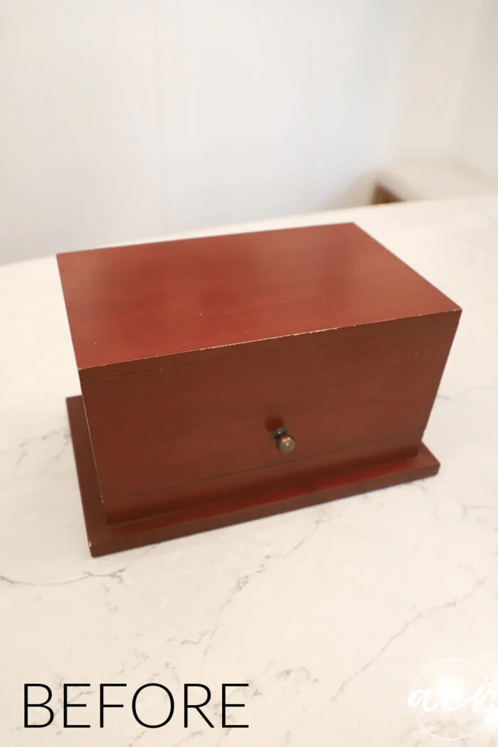 a rectangular wooden box with a dark reddish-brown finish sits on a white surface, its small round knob inviting curiosity. the word before appears in the bottom left corner, as if the box itself is waiting patiently, on island time.