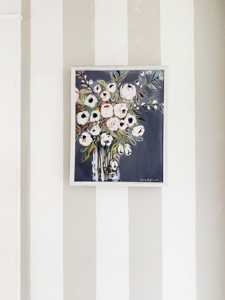 a framed painting of white and pink flowers in a glass vase hangs on a wall with wide vertical light gray and white stripes, adding a fresh touch to your hallway makeover.