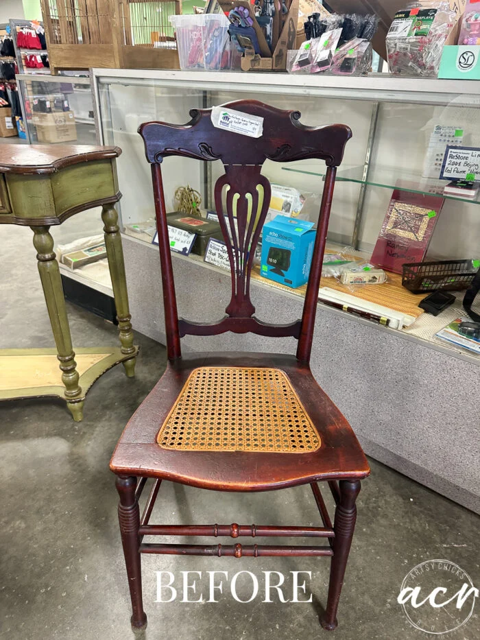 a vintage chair with a woven cane seat sits in front of a glass display case in a store. the word before is written at the bottom, highlighting this $9 chair before its stylish chair update.