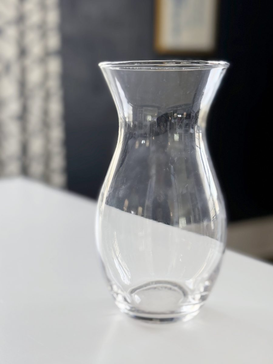 diy hobnail vase that looks like vintage milkglass 40 a clear, empty glass vase with a flared rim sits on a white surface, with a softly blurred, dark background and patterned window light visible on the left.