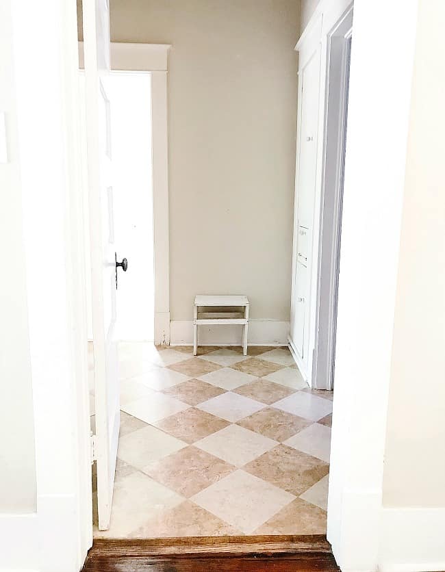 a bright hallway makeover with a checkerboard tile floor in shades of beige and white. there are open white doors on both sides, leading into different rooms, and a small white stool near the end of