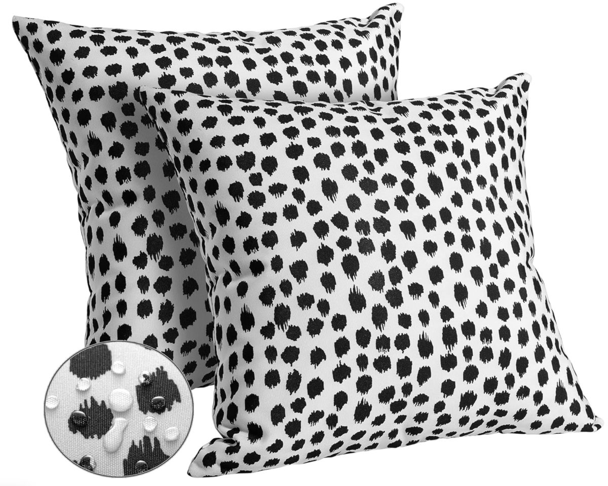 two white decorative pillows with black irregular polka dot patterns, shown overlapping. an inset circle highlights the fabric texture and dot detail up close.