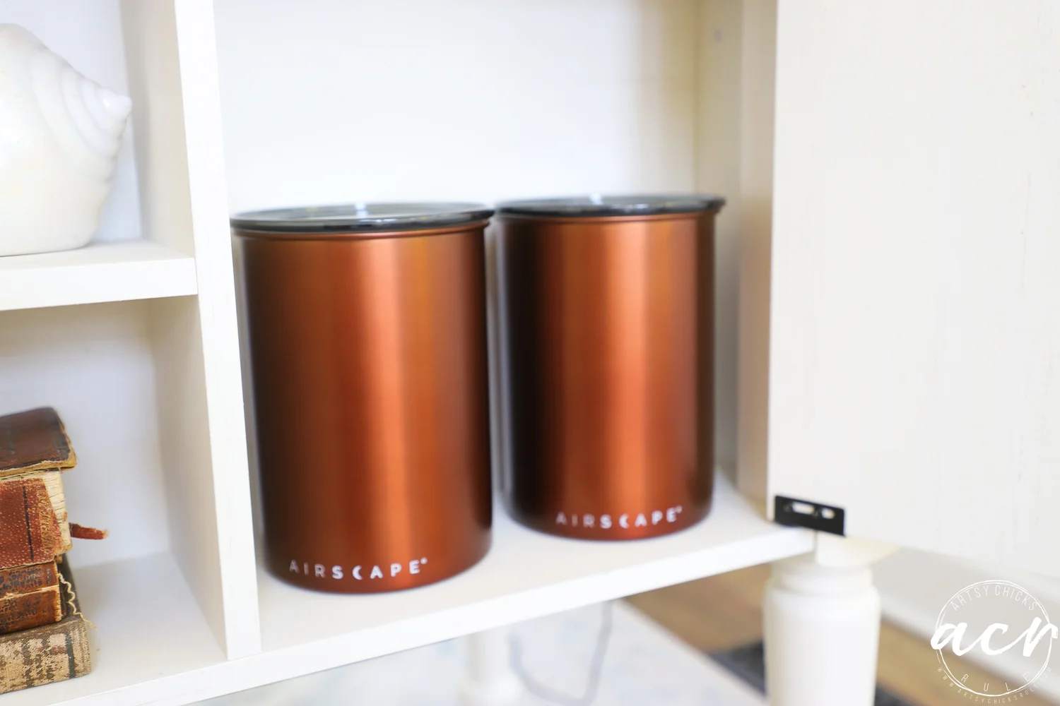 office reveal (sunroom) - artsy chicks rule® 69 two metallic brown canisters labeled airscrape sit side by side on a white shelf in the sunroom, with books and a shell visible nearby.