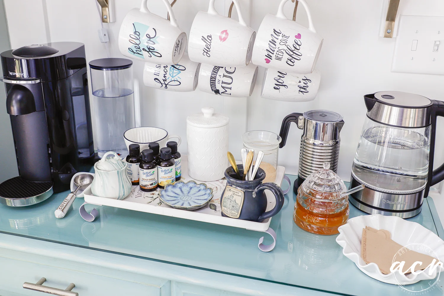 office reveal (sunroom) - artsy chicks rule® 72 a cozy coffee station in the sunroom features mugs hanging above, a coffee maker, electric kettle, glass honey jar, coffee syrups, sugar jar, plates, and utensils arranged on a blue countertop.
