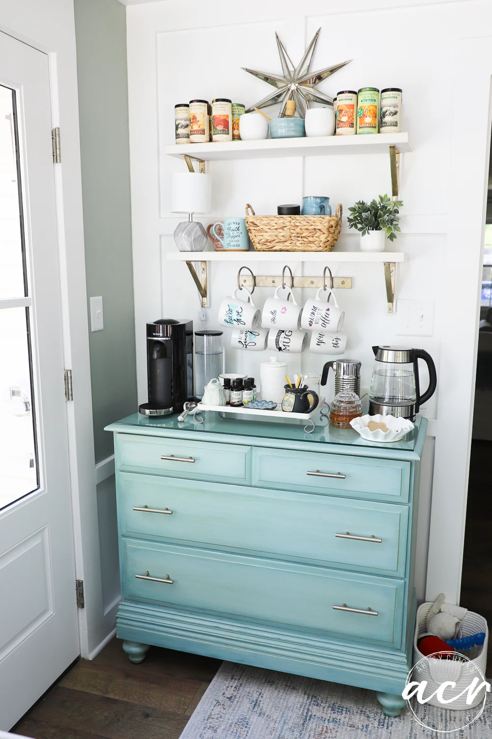 office reveal (sunroom) - artsy chicks rule® 70 a light blue dresser in the sunroom holds a coffee station with a coffee maker, mugs, glasses, and supplies. above, two white shelves display cans, mugs, a basket, and a plant. a starburst decor hangs on the white wall.