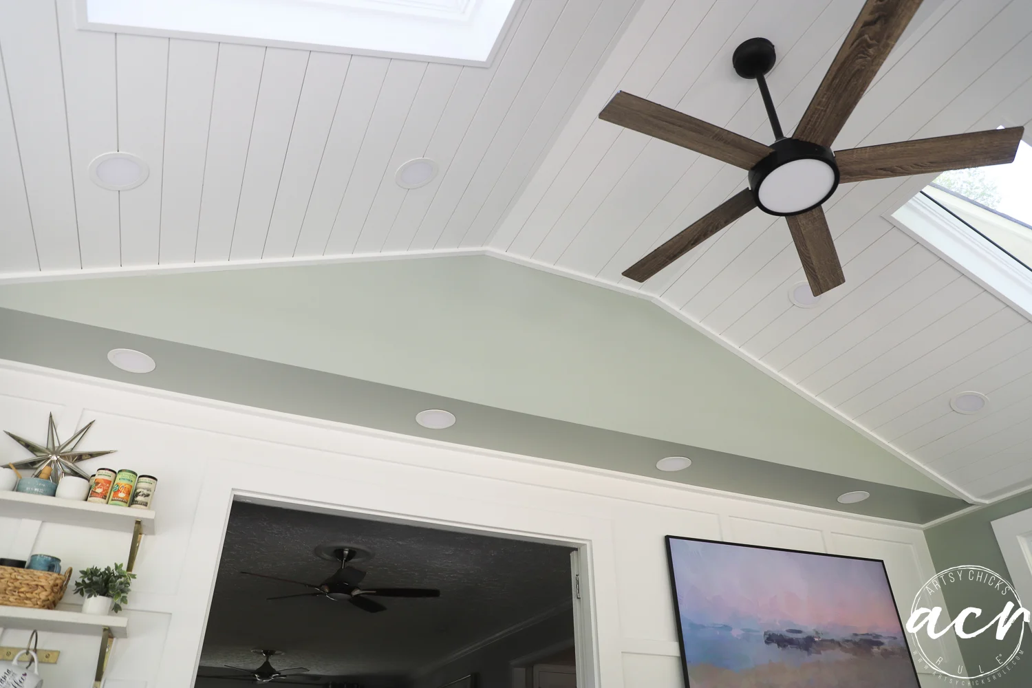 office reveal (sunroom) - artsy chicks rule® 80 a white shiplap vaulted ceiling with a modern wood ceiling fan, skylights, and recessed lights brightens this sunroom. below, a light green accent wall features shelves with decor and a landscape painting.