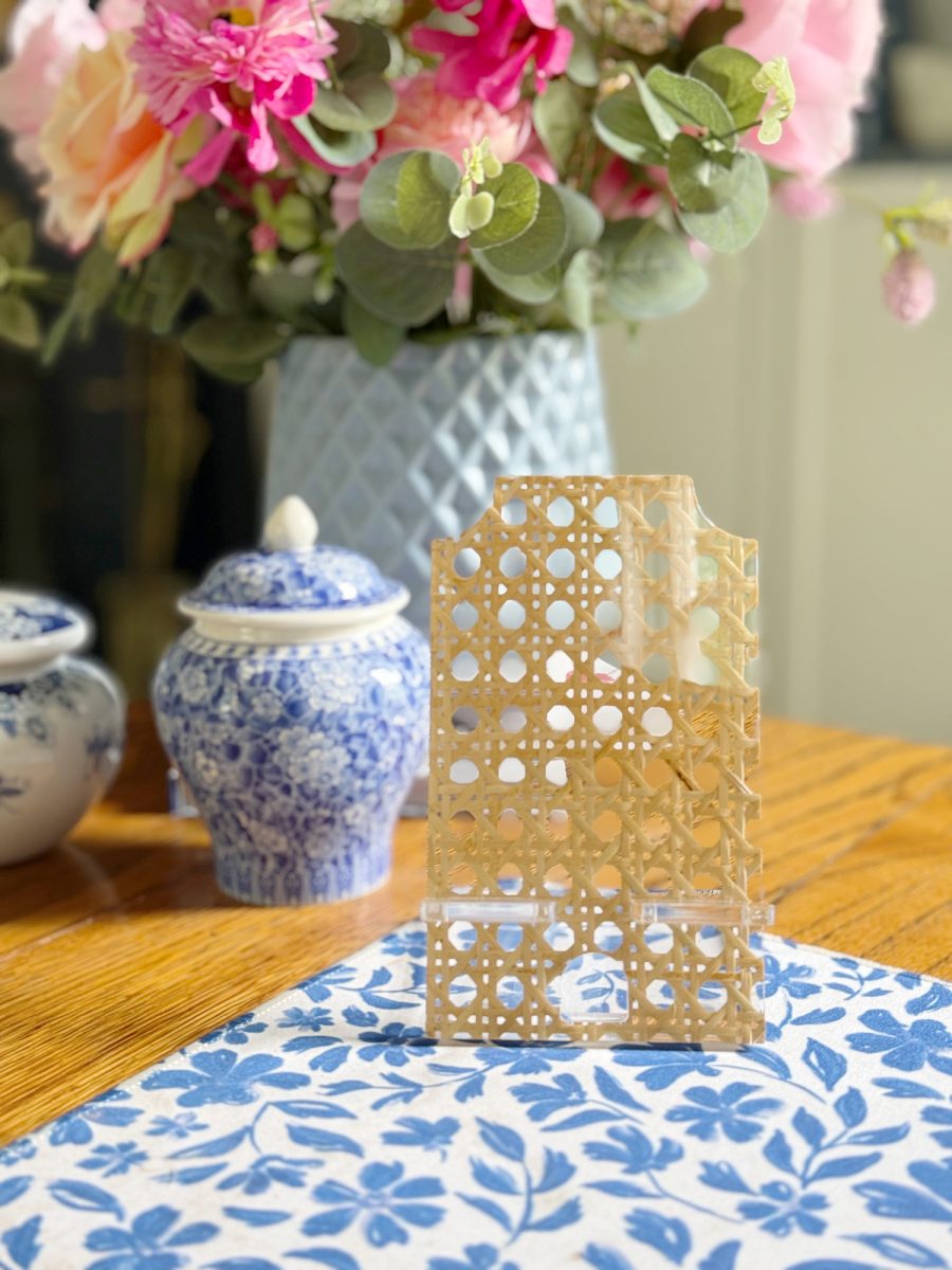 a decorative, lattice-patterned object sits on a blue and white floral placemat with a blue porcelain jar and a vase of colorful flowers in the background.