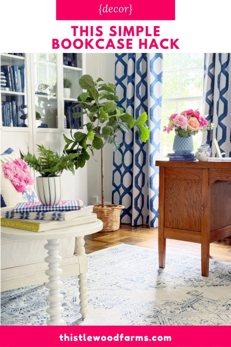 bright living room with a white coffee table, potted plant, wooden desk, and built-in bookshelves. blue and white decor, patterned curtains, and a floral arrangement add color. text overlay reads "this simple bookcase hack.