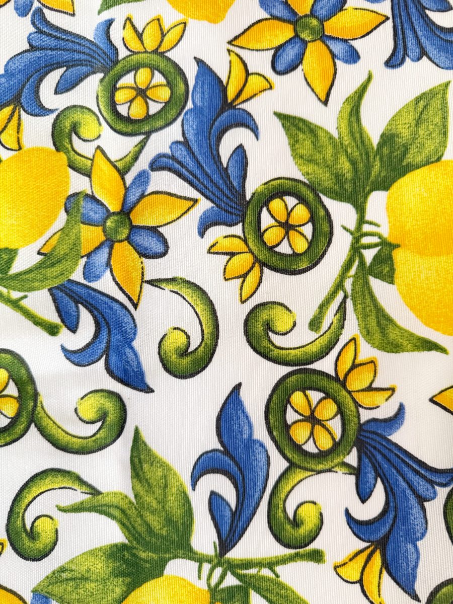 colorful fabric pattern featuring yellow lemons, green leaves, blue flowers, and swirling green vines on a white background. the design is vibrant and lively, with a mediterranean-inspired style.