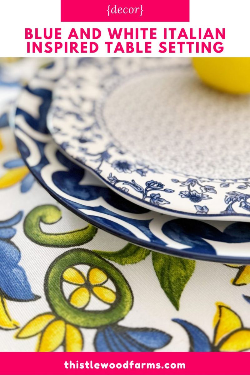 close-up of a blue and white patterned plate on a matching floral tablecloth with blue, green, and yellow designs, featuring a yellow lemon in the background. text reads, "italian inspiredtable setting in blue and white.