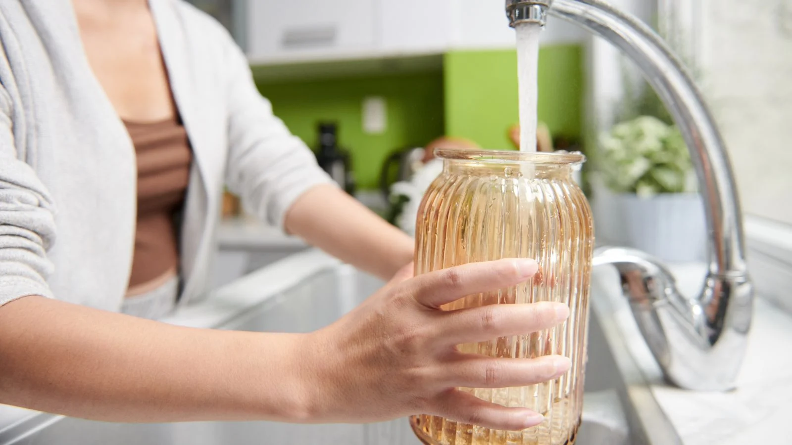 a close-up shot of a person in the process of filling a glass jar with clean tap water