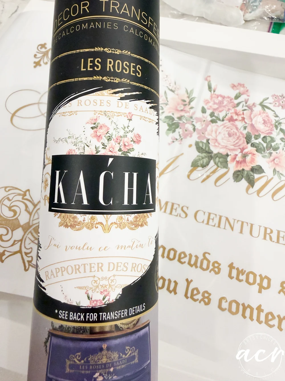 a close-up of a decorative kacha transfer sheet with floral and french text designs, featuring elegant roses and gold accents. in the background, a white thrift shop tray displays matching floral and gold lettering.