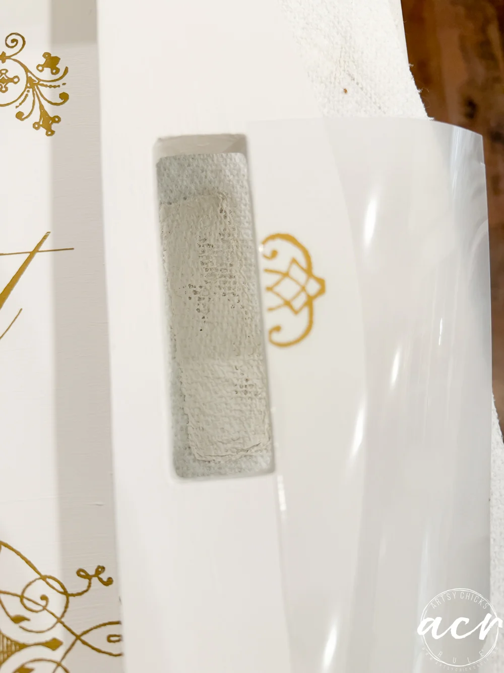 a hand uses a tool to apply a floral decal with pink flowers and green leaves onto a white tray from a thrift shop, accented by gold french text.