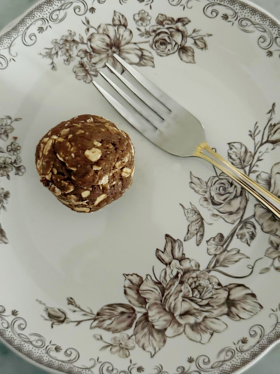 a decorative plate with floral patterns holds a metal fork and a single round ball made of oats and chocolate.