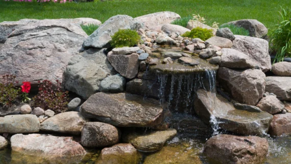 stacked stone water fountain surrounded by rocks in a garden landscape