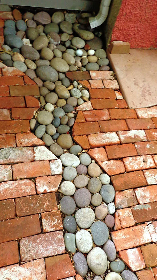 rock drainage bed beneath a downspout surrounded by landscaping stones in the shape of a river