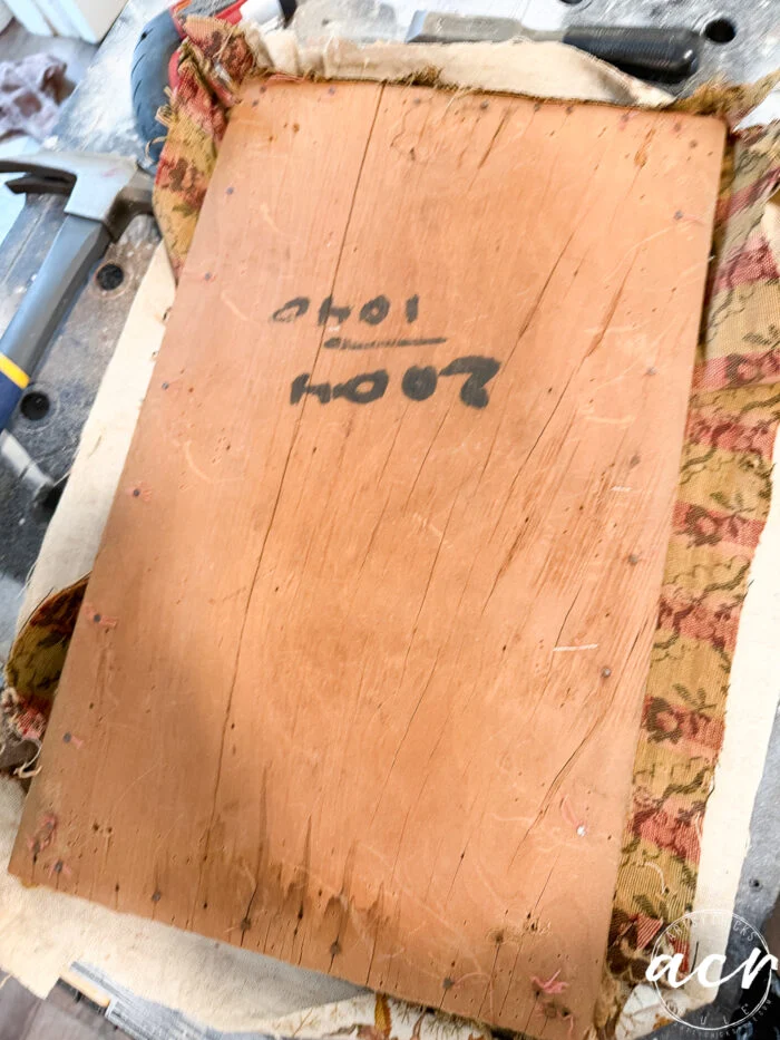 a vintage bench shows its age—a piece of worn wood with faded writing and numbers sits on old, patterned fabric, surrounded by tools and workshop materials, awaiting a thoughtful bench update.