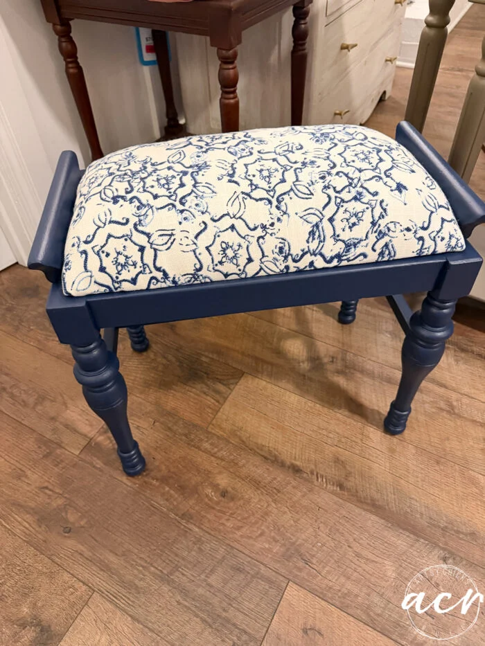 a small vintage bench with navy blue legs and frame, featuring a cushioned seat upholstered in cream fabric with a blue floral and abstract pattern, brings a charming furniture update to the wooden floor.